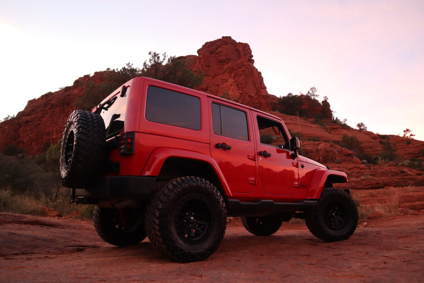 A red jeep is parked in front of a red rock.