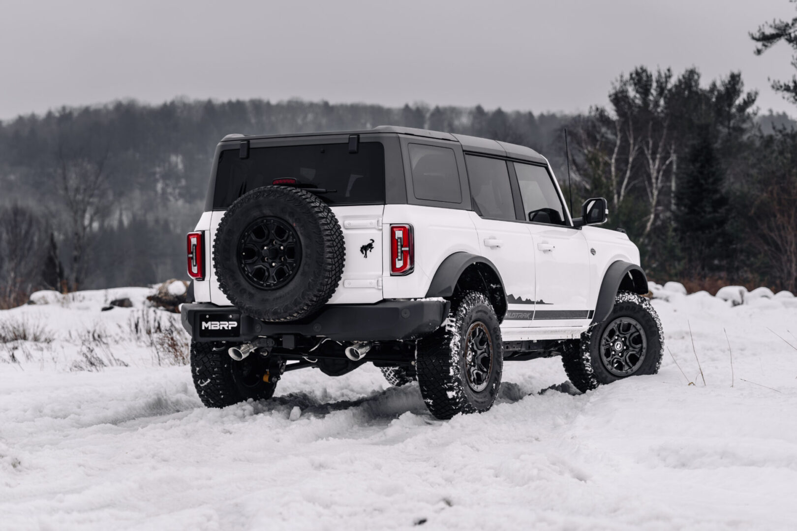 A white ford bronco is parked in the snow.