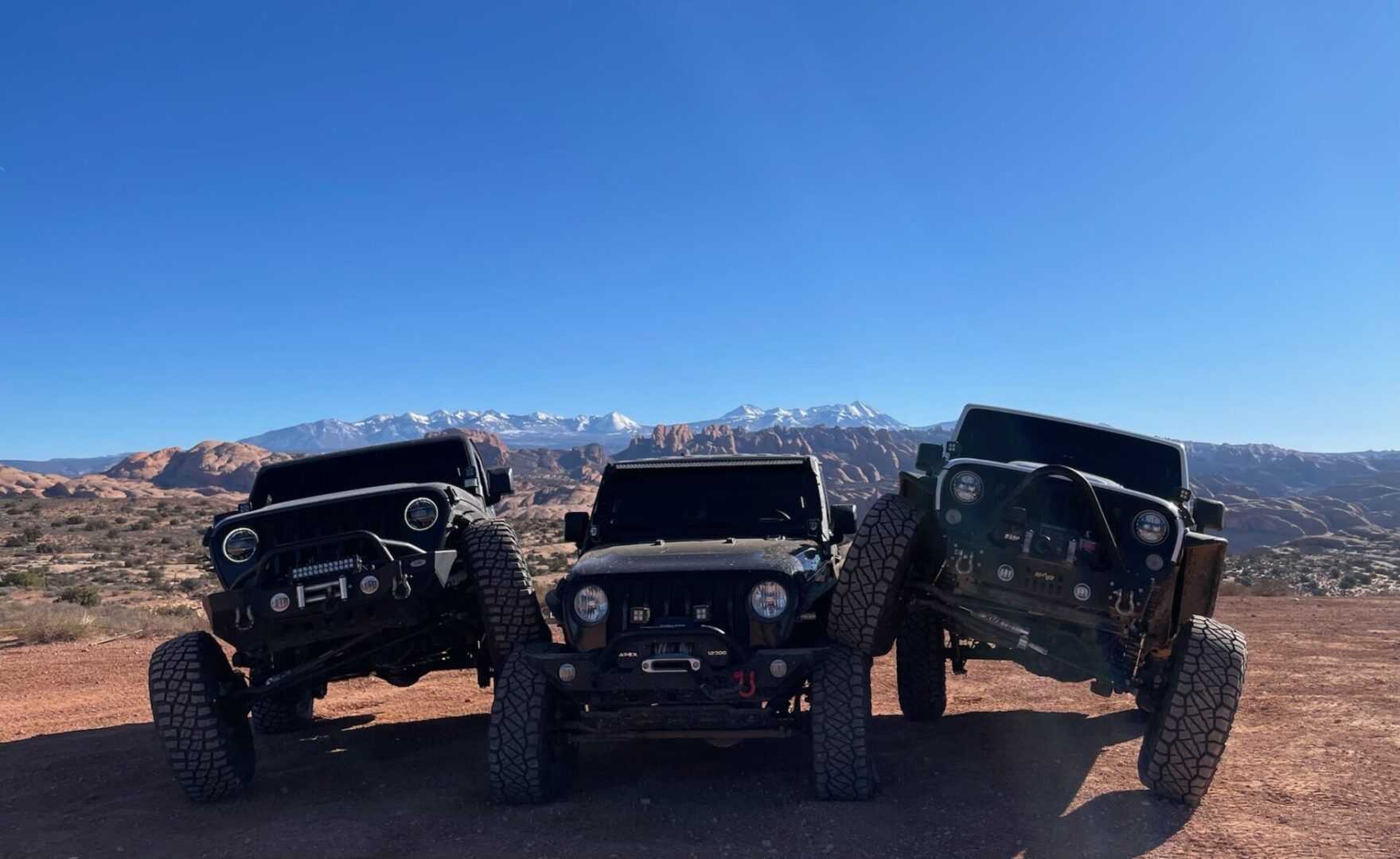 Three jeeps parked in the desert with mountains in the background.